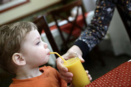 Child drinking orange juice from his mother handの写真素材