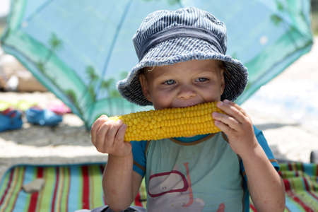 Boy in panama eating corn on picnic