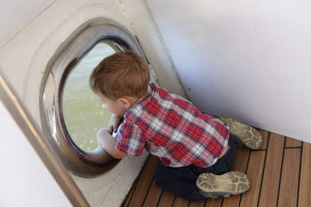 Child looking through porthole on ship deckの写真素材