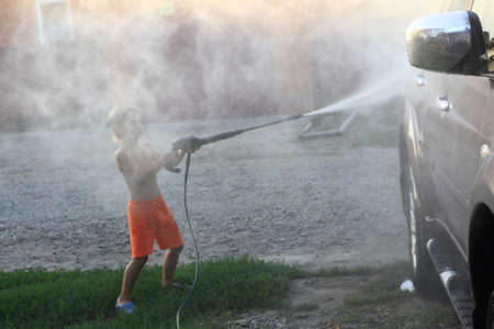 Boy washing car with high pressure washerの写真素材