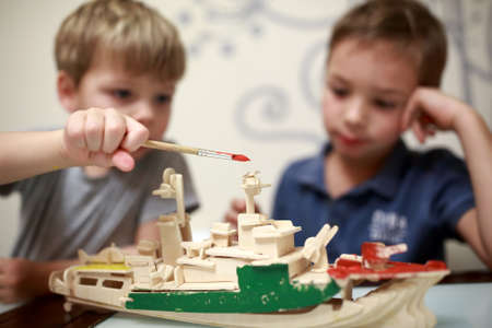 Kids painting wooden model of warship at home