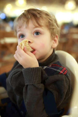 Boy eating pizza in highchair in cafeの写真素材