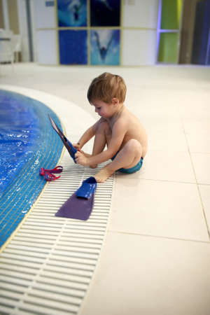 Child putting on flippers next to swimming poolの写真素材