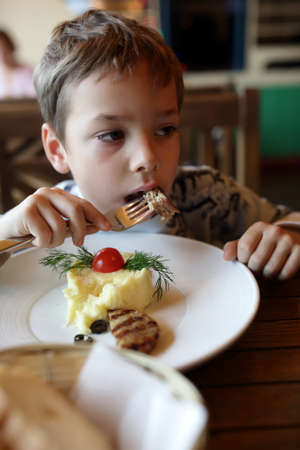 Kid eating cutlet at table in restaurantの写真素材