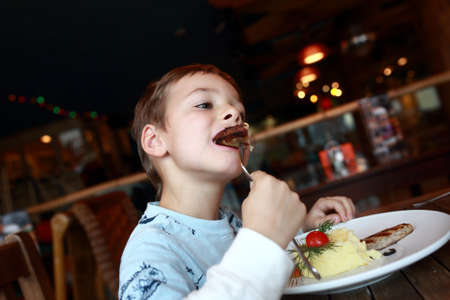 Boy eating cutlet at table in restaurantの写真素材