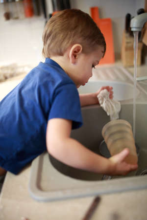 Kid washing dishes in kitchen at homeの写真素材