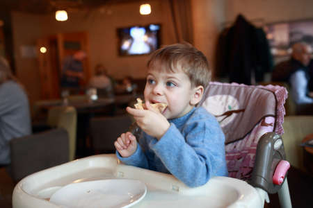 Kid eating pizza in highchair at cafeの写真素材