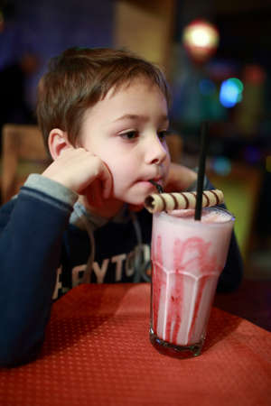 Child drinking milkshake at table in cafeの写真素材