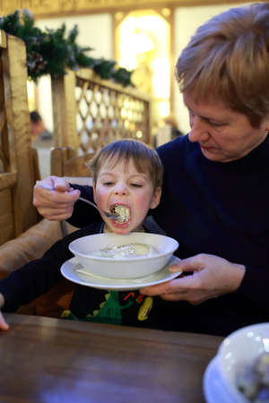 Grandmother feeding her grandson in a restaurantの写真素材