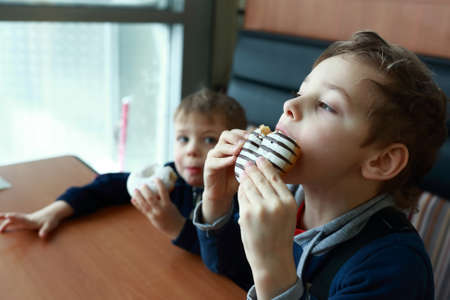 Brothers eating donuts at table in cafeの写真素材