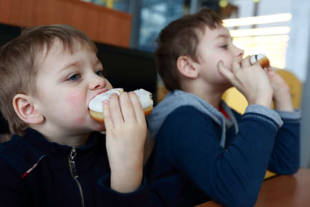 Two brothers eating donuts at table in cafeの写真素材