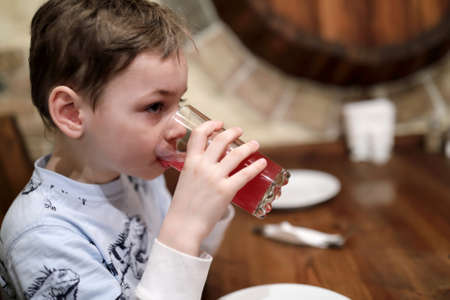 Child drinking juice at table in cafeの写真素材
