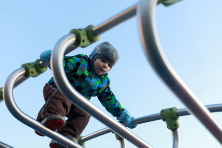 Boy climbing metal bridge at playground in spring