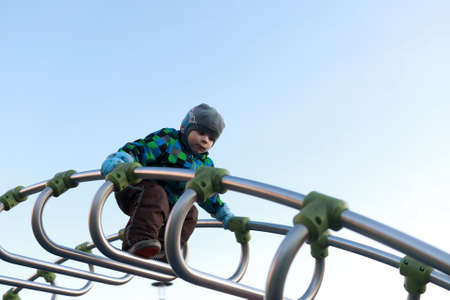 Kid climbing metal bridge at playground in spring