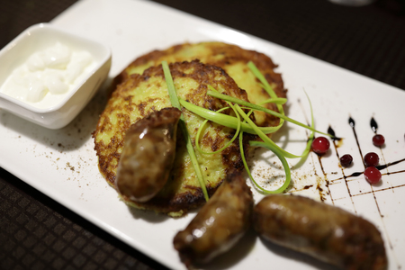 Sausages and potato pancakes on white plate in restaurantの写真素材