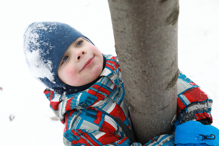Boy hugging tree trunk in winter parkの写真素材