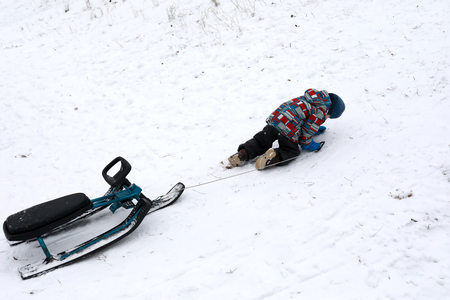 Boy pulls snow scooter on hill in winterの写真素材