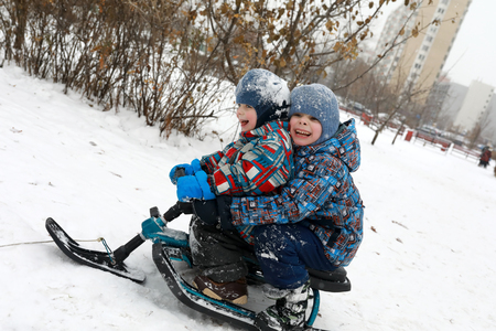 Brothers sitting on snow scooter in winter parkの写真素材