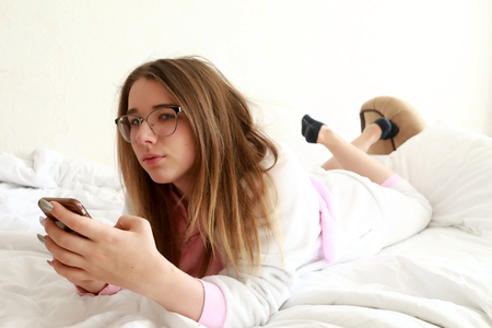 Teenager with smartphone lying on bed in the morningの写真素材