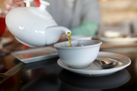 Person pouring tea from white teapot in restaurantの写真素材