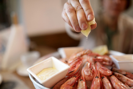 Person squeezes lemon juice on shrimps in restaurantの写真素材