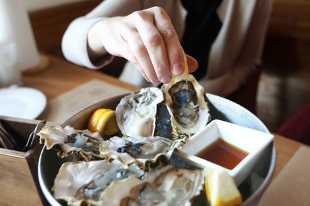 Person squeezes lemon juice on oysters in restaurantの写真素材