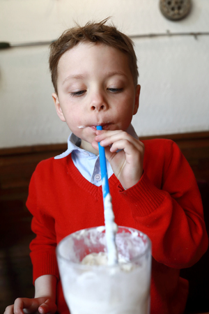 Child drinking milkshake at table in restaurantの写真素材