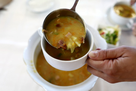 Person pouring pea soup into bowl in restaurantの写真素材