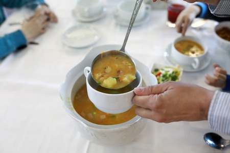Person pouring soup into bowl in restaurant