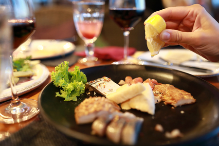 Person sprinkles fish with lemon juice in restaurantの写真素材