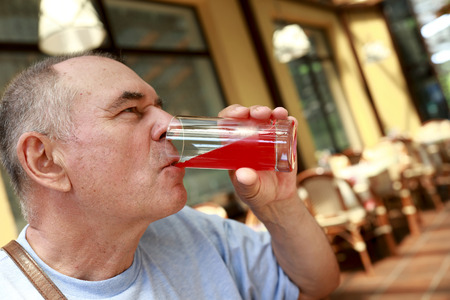 Senior man drinking juice in outdoor cafe