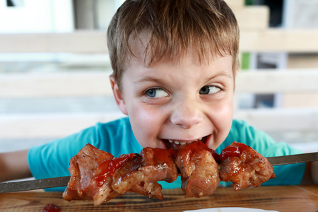Child eating pork neck kebab with ketchupの写真素材