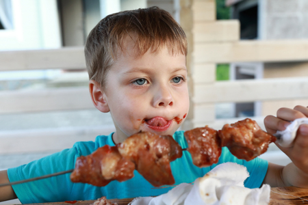 Kid eating pork neck kebab with ketchupの写真素材