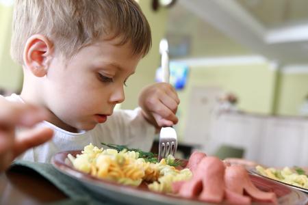 Child has pasta with sausages in restaurantの写真素材