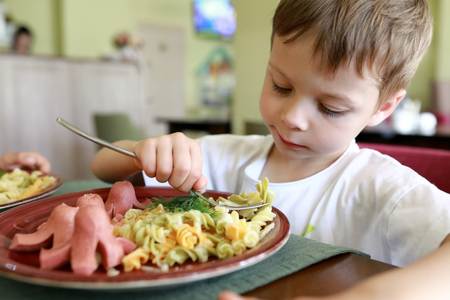 Boy eating pasta with sausages in restaurantの写真素材