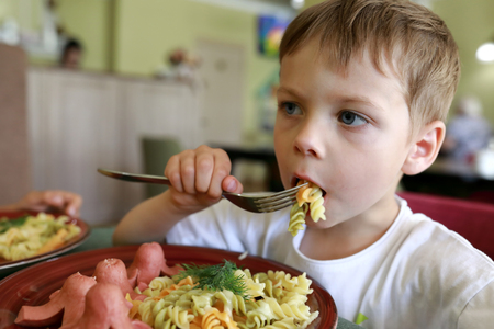 Kid eating pasta with sausages in restaurantの写真素材