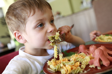 Kid has pasta with sausages in restaurantの写真素材