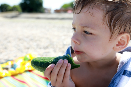 Child has raw cucumber on the beachの写真素材
