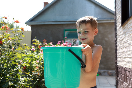 Child catches drops of water with bucket in backyardの写真素材