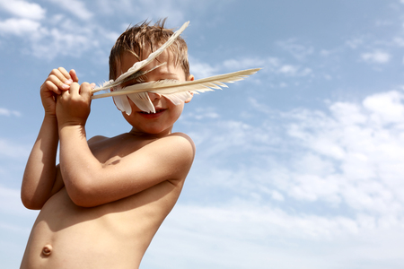 Portrait of boy with bird feathers on sky backgroundの写真素材