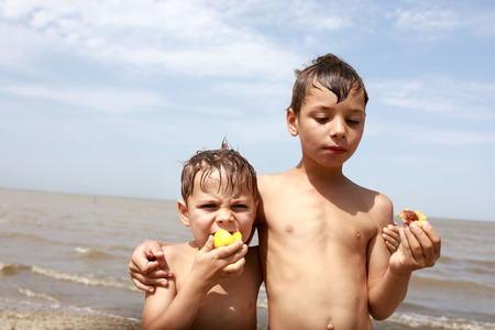 Children eat peaches on beach in summerの写真素材