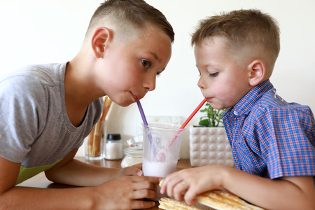 Brothers drinking vanilla milkshake in a cafeの写真素材