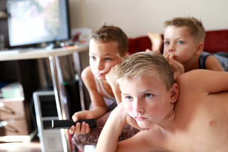 Three brothers watching TV on sofa at homeの写真素材