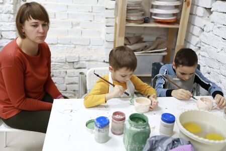 Family painting clay mugs in pottery workshop