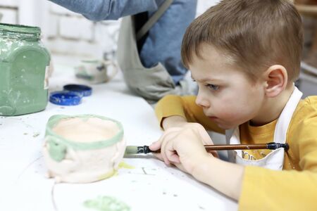 Kid paints clay mug in pottery workshopの写真素材