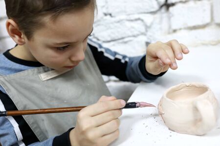 Child painting clay pot in pottery workshopの写真素材