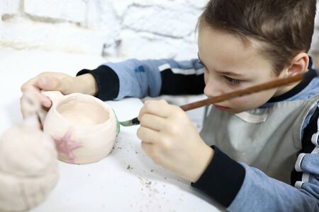 Child painting clay cup in pottery workshopの写真素材