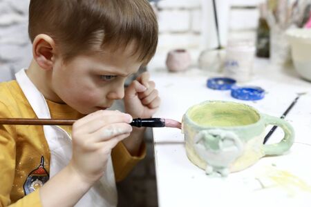 Boy paints clay cup in pottery workshopの写真素材