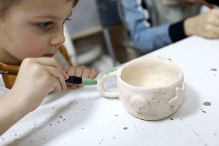 Boy painting clay mug in pottery workshopの写真素材