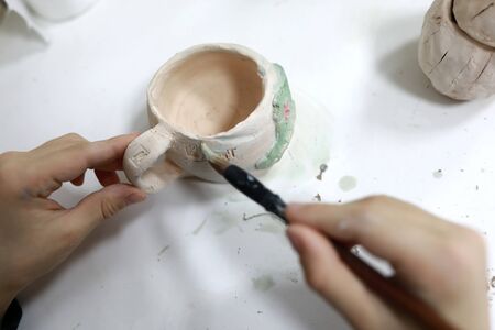 Person painting clay cup in pottery workshop